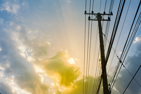 Silhouette, Pole with power lines lies across. The light shines in the evening sky backdrop, with...
