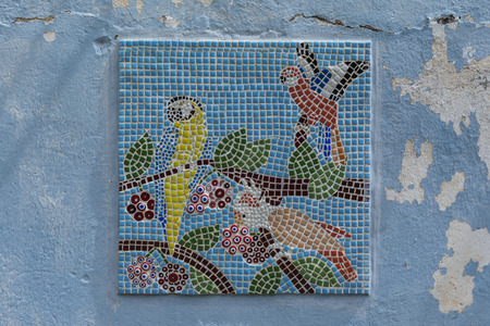 Fragment of a blue painted wall with a mosaic showing tropical birds