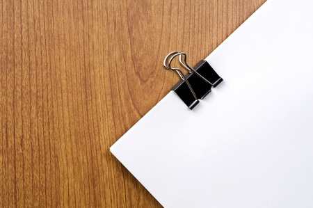 Black clip and blank paper on wooden desk の写真素材