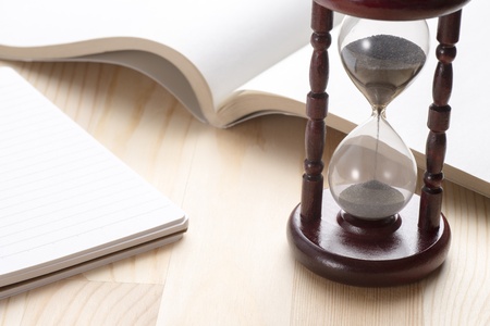 hourglass and open book on wooden table