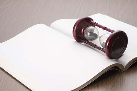 hourglass and open book on wooden table