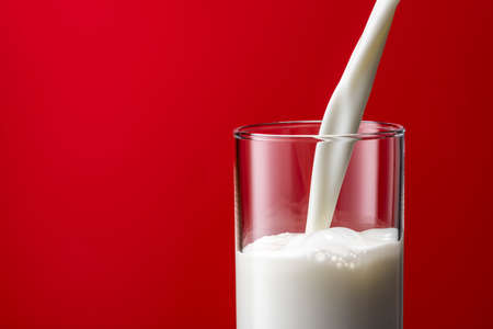 Pouring milk into a glass, red backgroundの写真素材