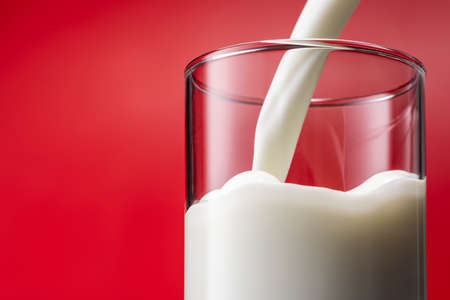 Pouring milk into a glass, red backgroundの写真素材