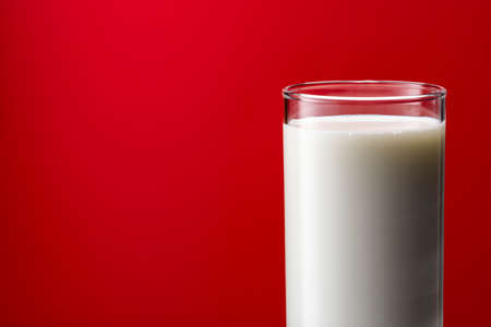 Pouring milk into a glass, red backgroundの写真素材