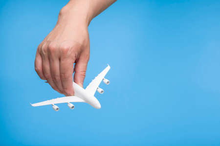 Hand holding airplane model on light blue background.
