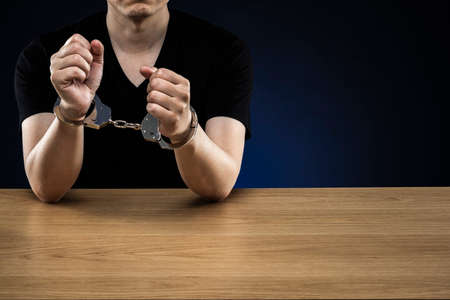 Handcuffed men, on wood grain table.の写真素材