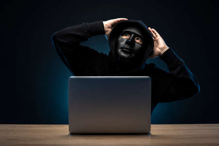 Mysterious man wearing a mask. Open laptop.