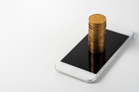 Smartphone with coins stacked on white background.の写真素材