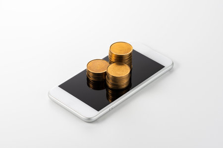 Smartphone with coins stacked on white background.の写真素材