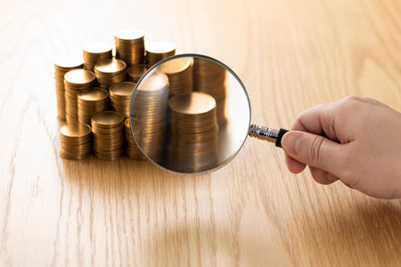 Magnifier and coins stacked on wooden table.