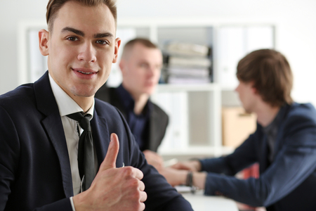 Handsome smiling man showing OK or approval sign with thumb up in creative people office portrait. High level and quality service, job offer, excellent education, advisor, serious business conceptの写真素材