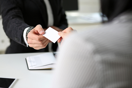 Male hand in suit give blank calling card to female visitor closeup. White collar partners company name exchange, executive or ceo introducing at conference, product consultant, sale clerk conceptの写真素材