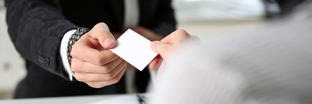 Male hand in suit give blank calling card to female visitor closeup. White collar partners company name exchange, executive or ceo introducing at conference, product consultant, sale clerk conceptの写真素材