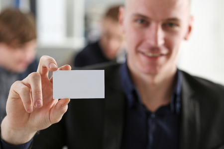 Smiling Businessman in suit hold in hand blank calling card closeup. White collar partners company name exchange, executive or ceo introducing at conference, product consultant, sales clerk conceptの写真素材