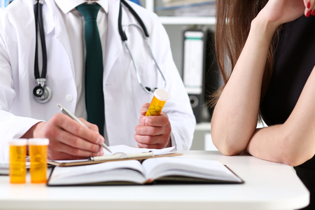 Male medicine doctor hand hold jar of pills and write prescription to patient at worktable. Panacea and life save, prescribing treatment, legal drug store concept. Empty form ready to be usedの写真素材