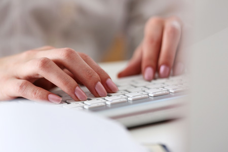 Female hands typing on silver keyboard using computer pc at workplace closeup. White collar job,...