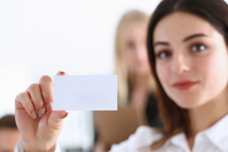 Smiling Business woman in suit hold in hand blank calling card closeup. White collar partners company name exchange, executive or ceo introducing at conference, product consultant, sales clerk conceptの写真素材