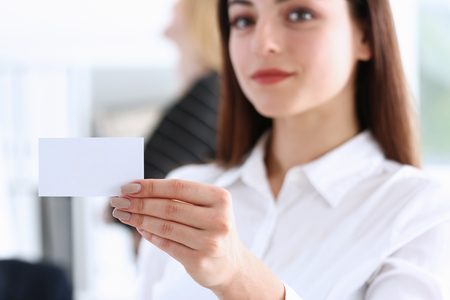 Smiling Business woman in suit hold in hand blank calling card closeup. White collar partners company name exchange, executive or ceo introducing at conference, product consultant, sales clerk conceptの写真素材