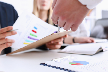 Group of people deliberate on problem with clipboard pad closeup. White collar check money papers, stock exchange market, earnings list, partnership agreement discussion conceptの写真素材