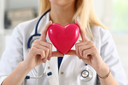 Female medicine doctor hands holding and covering red toy heart closeup. Cardio therapeutist, student education, physician make cardiac physical, heart rate measure, arrhythmia conceptの写真素材