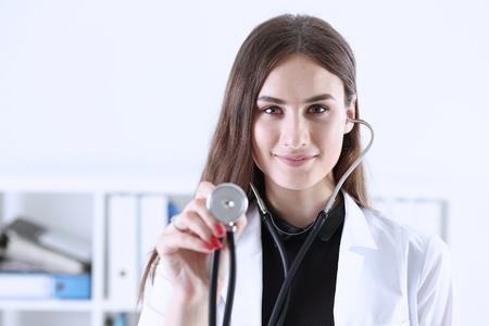 Beautiful smiling female doctor hold in hand stethoscope head going to listen patient. Medic shop or store, physical, disease prevention, er consultant, 911, pulse measure, healthy lifestyle conceptの写真素材
