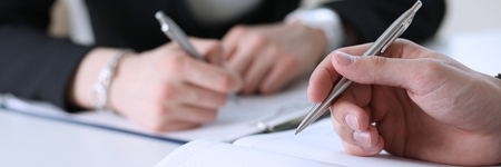 Group of people hold silver pen ready to make note in opened notebook sheet closeup. Training course, university practice homework, school or college exercise, secretary table management conceptの写真素材