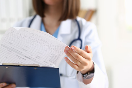 Female medicine doctor hand holding silver pen looking in clipboard pad closeup. Ward round, patient visit check, 911, medical calculation and statistics concept. Physician ready to examine patientの写真素材