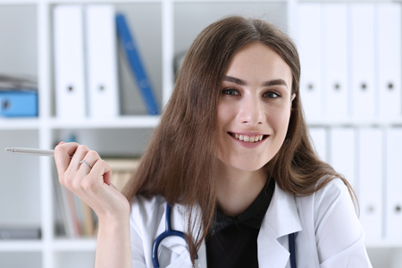 Beautiful smiling female doctor sit at workplace. Physical and disease prevention, patient aid, exam visit, 911, ward round, prescribe remedy, healthy lifestyle, consultant profession conceptの写真素材