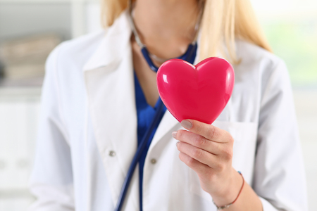 Female medicine doctor hands holding and covering red toy heart closeup. Cardio therapeutist, student education, physician make cardiac physical, heart rate measure, arrhythmia conceptの写真素材