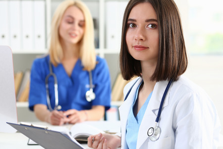 Beautiful smiling female doctor hold clipboard pad and fill something with silver pen. Physical, illness prevention, prescribe remedy, ward round, therapeutist assistance, healthy lifestyle conceptの写真素材