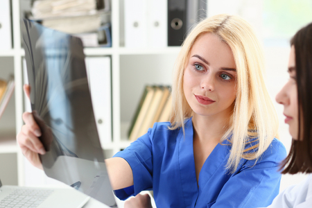 Group of beautiful female doctors hold in hand and look at xray photography to detect problem. Bone disease exam, medic assistance, cancer aid, healthy lifestyle, ill test, hospital practice conceptの写真素材