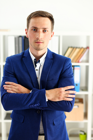 Handsome man in suit and tie stand in office looking in camera hands crossed on chest. White collar dress code, modern office lifestyle, graduate college study, profession idea, coach train conceptの写真素材
