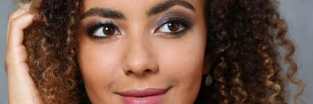 A beautiful black woman with a large face portrait. On a gray background a smiling beauty fashion style mulatto curly hair with white locks eye view of the cameraの写真素材