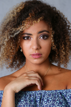 A beautiful black woman portrait. Tests the emotion of bewilderment of fear of terror confusion beauty fashion style mulatto curly hair with white locks eye view of the cameraの写真素材