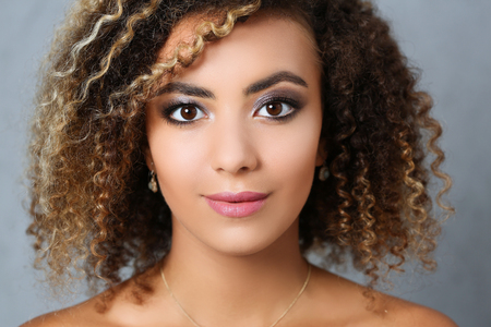 A beautiful black woman with a large face portrait. On a gray background a smiling beauty fashion style mulatto curly hair with white locks eye view of the cameraの写真素材