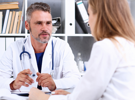Smiling handsome mature doctor communicate with patient holding silver pen and pad. Physical agreement signature, disease prevention, consent sign, 911, prescribe remedy, healthy lifestyle conceptのeditorial素材