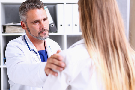 Friendly male doctor hold patient shoulder in office during reception. Examination result, positive test, calm down, promise and cheer up, grief and suffer, treatment, condolence, ethics conceptの写真素材