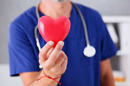Male doctor wearing blue uniform hold in arms red toy heart closeup. Cardio therapeutist, student education, CPR, 911 life save, physician make cardiac physical, pulse rate measure, arrhythmiaの写真素材