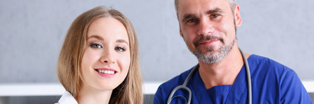 Smiling handsome doctor communicate with patient holding silver pen and showing pad. Physical agreement signature, disease prevention, consent sign, 911, prescribe remedy, healthy lifestyle conceptの写真素材