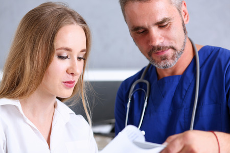 Smiling handsome doctor communicate with patient holding silver pen and showing pad. Physical agreement signature, disease prevention, consent sign, 911, prescribe remedy, healthy lifestyle conceptのeditorial素材