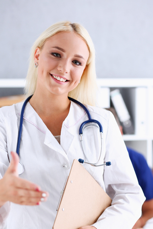 Female medicine doctor hold pad and give arm to shake in office portrait. Friend welcome, introduction or thanks gesture, test work, examine patient, congratulation, help exam, teamwork deal conceptのeditorial素材