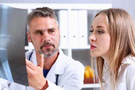 Mature male doctor hold in arm and look at xray photography discussing it with female patient portrait. Bone disease exam, medic assistance, cancer test, healthy lifestyle, hospital practice conceptの写真素材