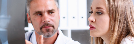 Mature male doctor hold in arm and look at xray photography discussing it with female patient portrait. Bone disease exam, medic assistance, cancer test, healthy lifestyle, hospital practice conceptの写真素材