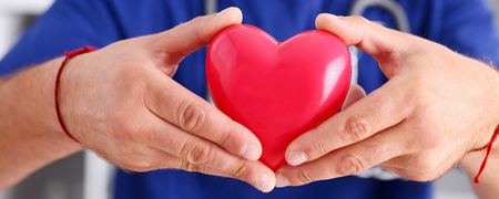 Male doctor wearing blue uniform hold in arms red toy heart closeup. Cardio therapeutist, student education, CPR, 911 life save, physician make cardiac physical, pulse rate measure, arrhythmiaの写真素材