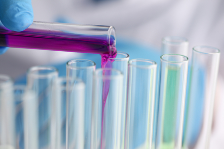 A male chemist holds test tube of glass in his hand overflows a liquid solution of potassium permanganate conducts an analysis reaction takes various versions of reagents using chemical manufacturingの写真素材