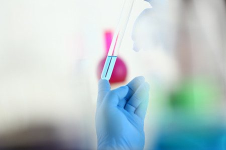 A male chemist holds test tube of glass in his hand overflows a liquid solution of potassium permanganate conducts an analysis reaction takes various versions of reagents using chemical manufacturingの写真素材
