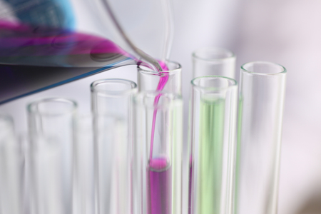 A male chemist holds test tube of glass in his hand overflows a liquid solution of potassium permanganate conducts an analysis reaction takes various versions of reagents using chemical manufacturingの写真素材