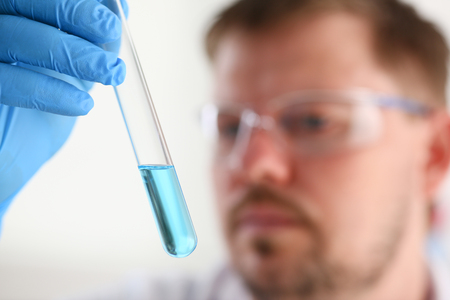 A male chemist holds test tube of glass in his hand overflows a liquid solution of potassium permanganate conducts an analysis reaction takes various versions of reagents using chemical manufacturingの写真素材