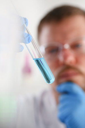 A male chemist holds test tube of glass in his hand overflows a liquid solution of potassium permanganate conducts an analysis reaction takes various versions of reagents using chemical manufacturingの写真素材