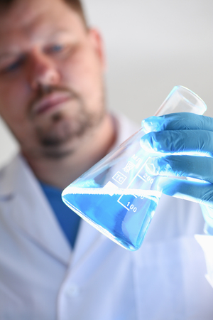 A male chemist holds test tube of glass in his hand overflows a liquid solution of potassium permanganate conducts an analysis reaction takes various versions of reagents using chemical manufacturingの写真素材